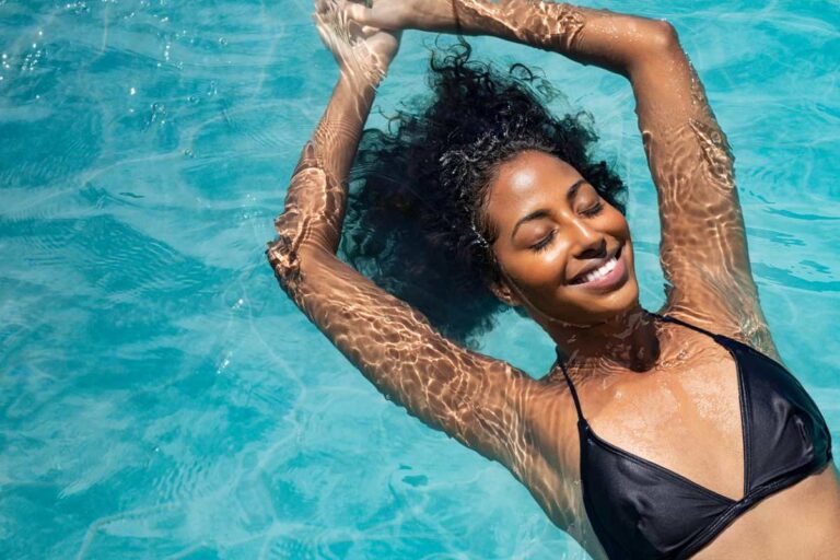 A happy woman smiles as she swims luxuriously through her pool