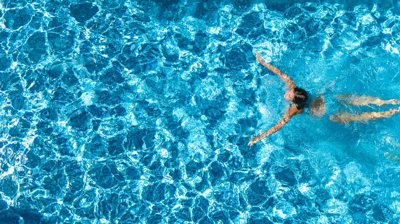 A woman swims through her pool for cardio exercise.